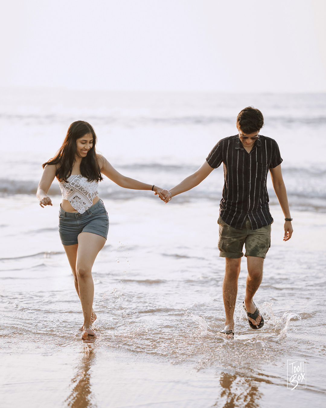 Dipti and Akash holding hands as they walk through the waves