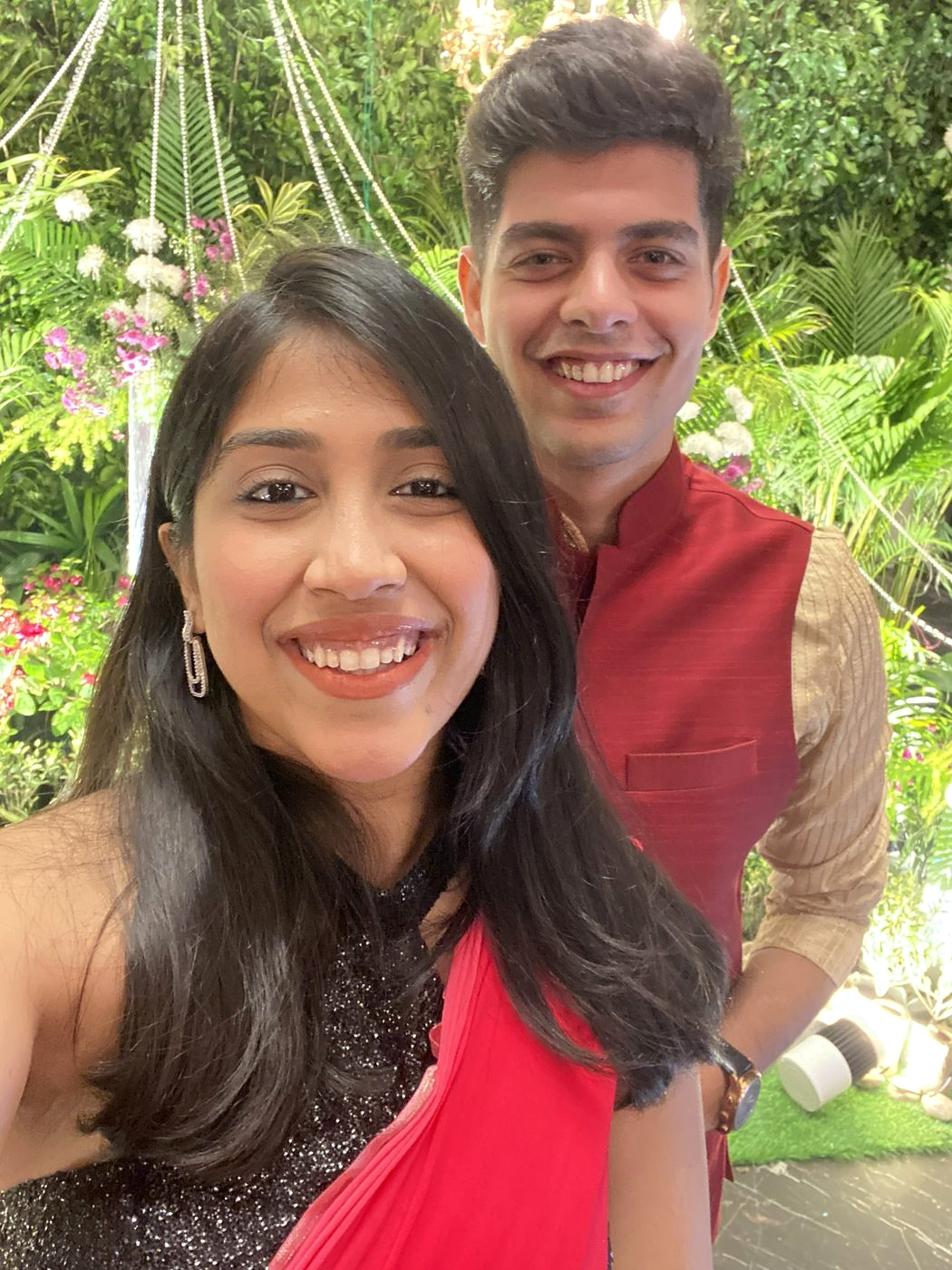 Dipti and Akash at a garden celebration, she in red, he in a red nehru jacket
