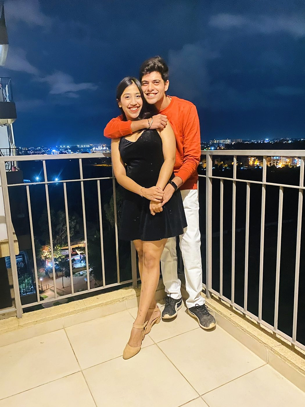 On a rooftop at dusk with the city lights behind them
